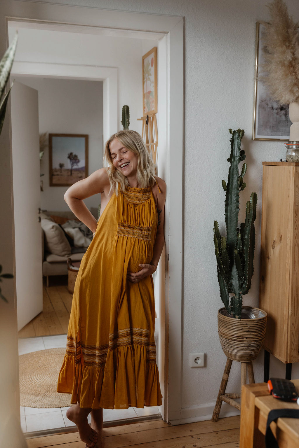 pregnant woman in a long yellow dress leaning against a door frame smiling eyes closed