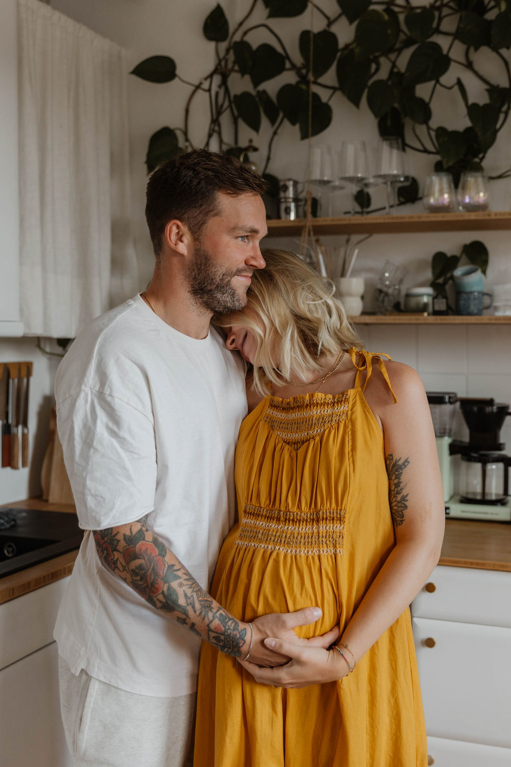 couple standing in a kitchen woman is pregnant leaning her head on her partner's shoulder