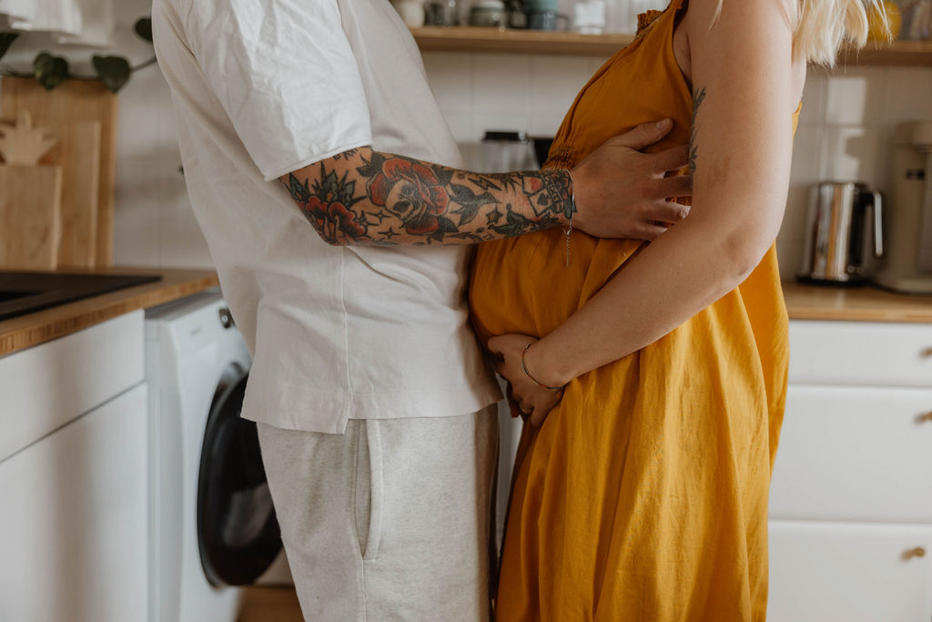 couple turned to each other standing in a kitchen woman is holding her pregnant belly husband is holding on to her side