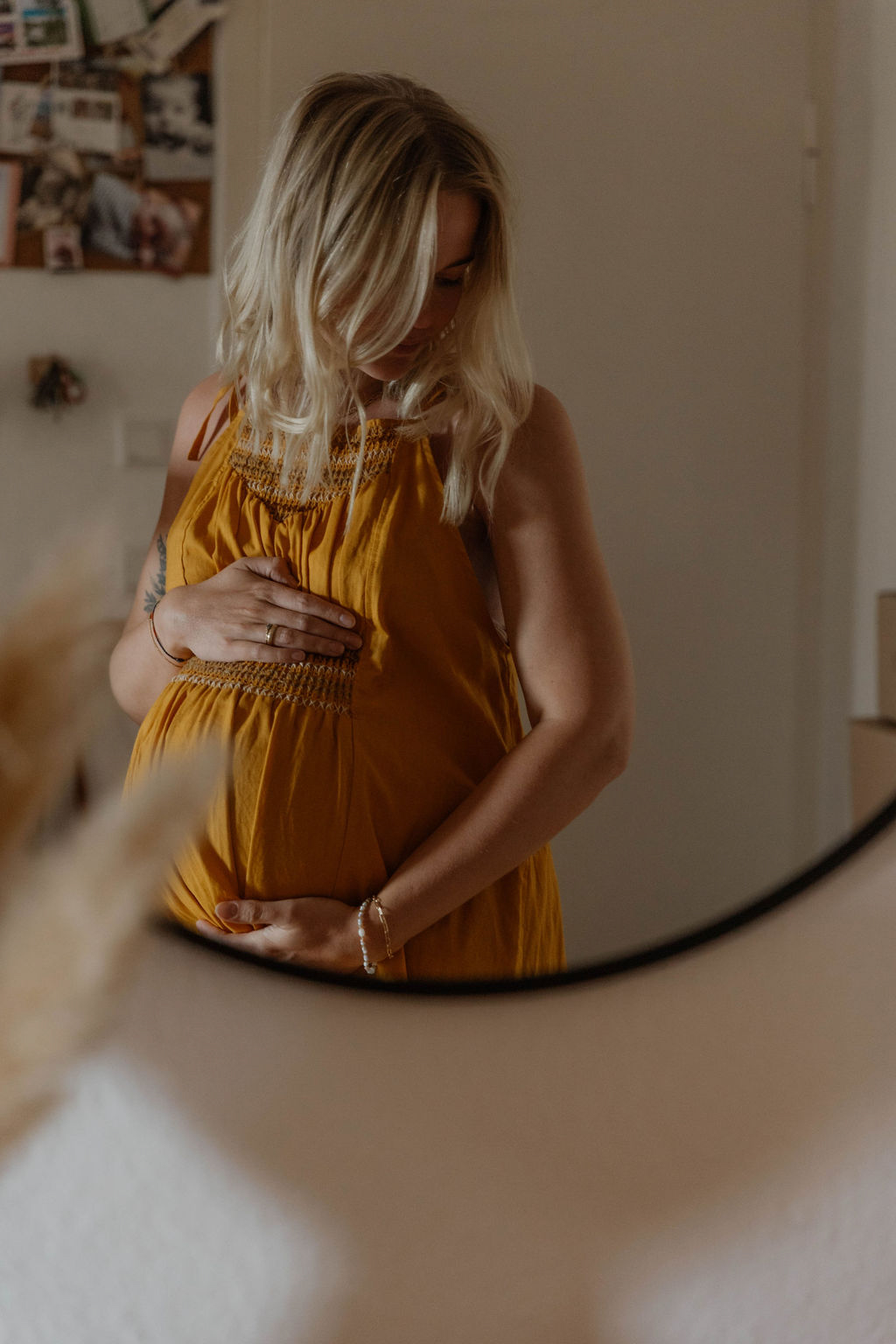 pregnant woman photographed in a mirror holding her belly looking down to the side