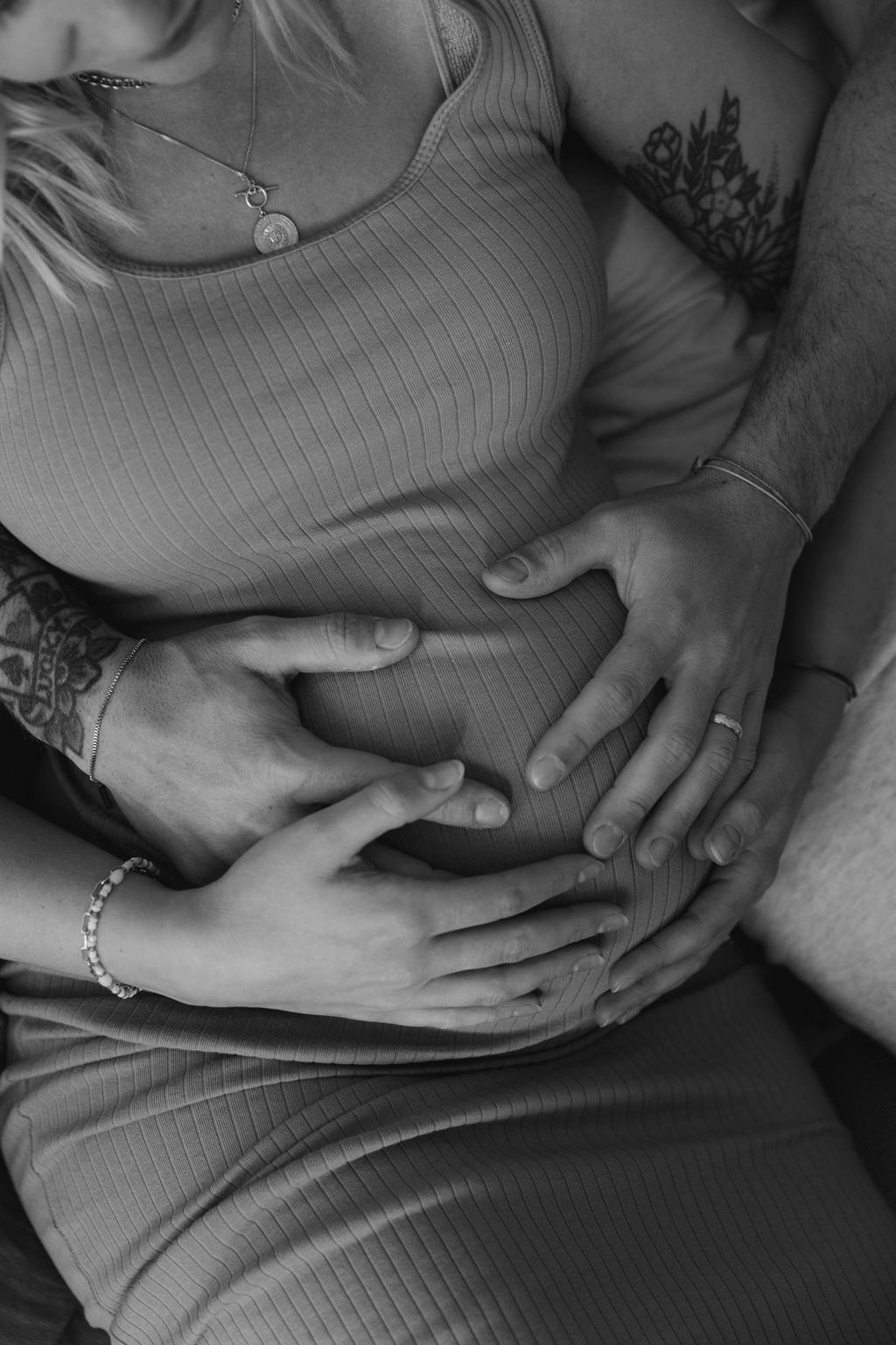 black and white photo close up woman's pregnant belly her and the father's hands are placed on it
