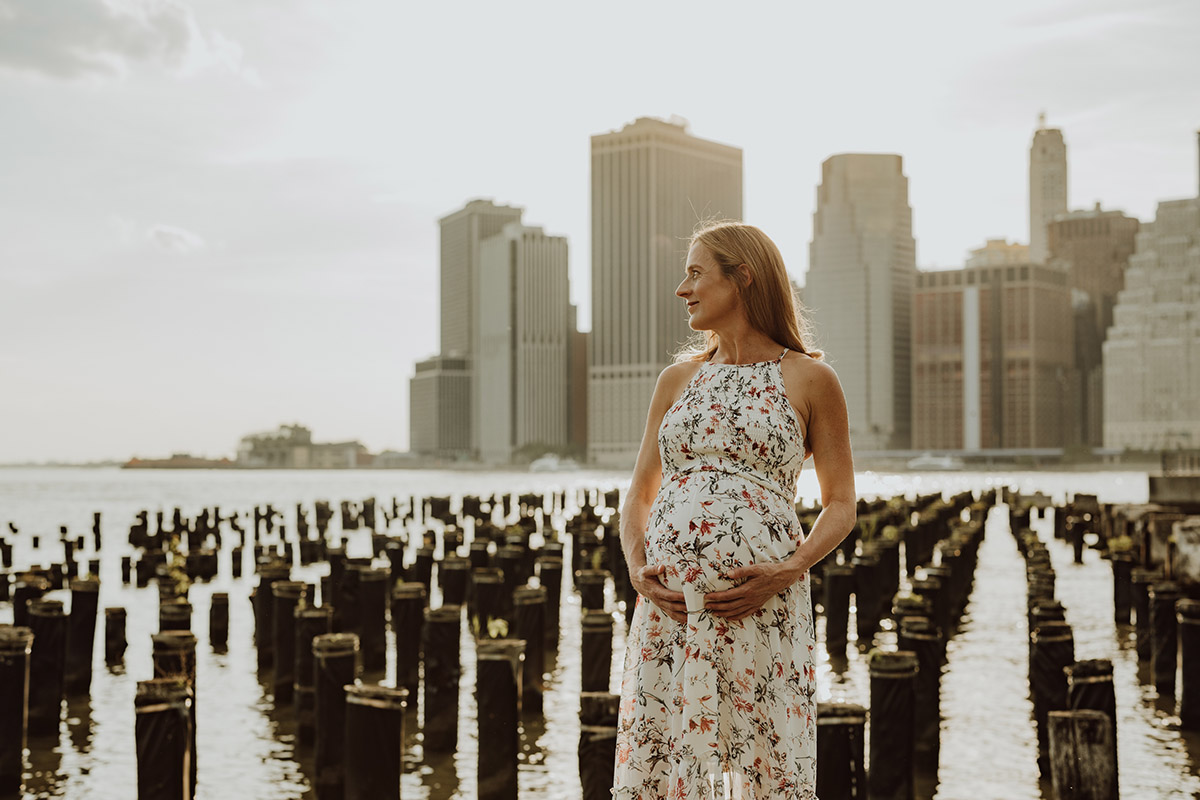 pregnant woman standing by the east river with new york skyline in the background