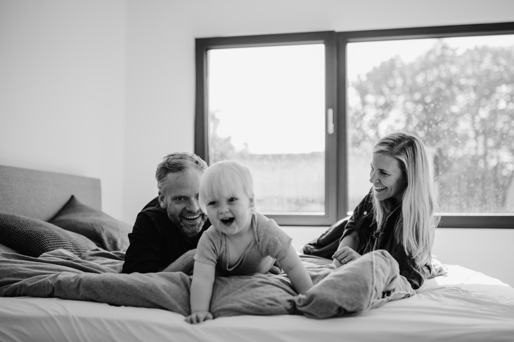black and white photo family of three lying on a bed all laughing