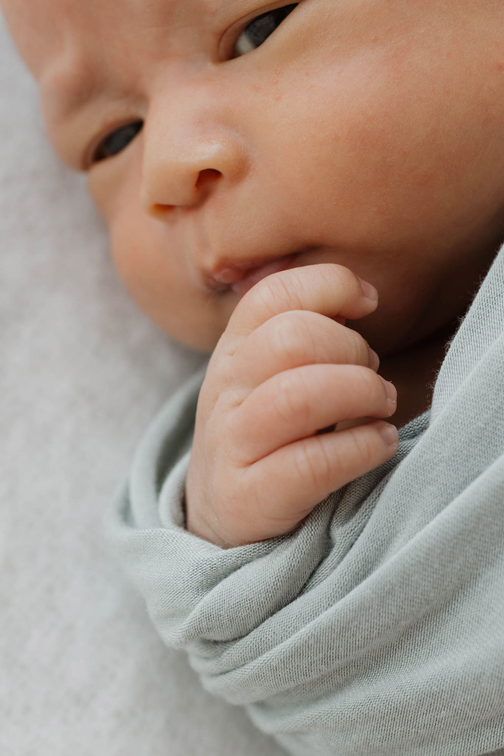 close up of a baby wrapped in a grey blanket hand sticking out