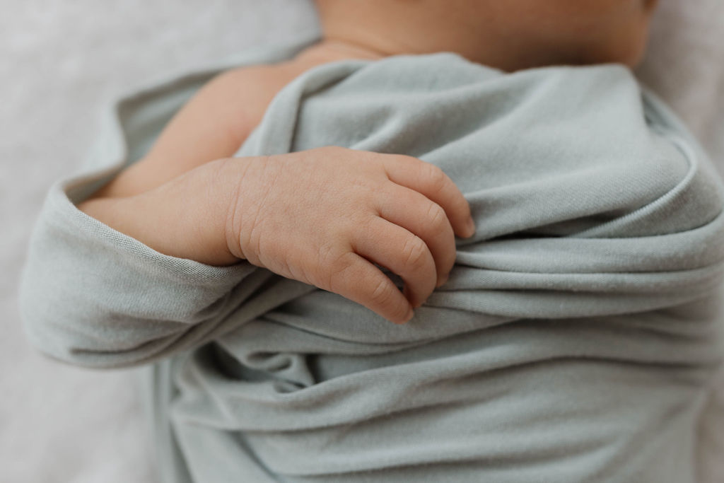 close up of a baby's hand sticking out of a grey blanket