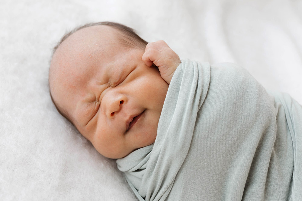 close up of a baby wrapped in a grey blanket squinting its eyes