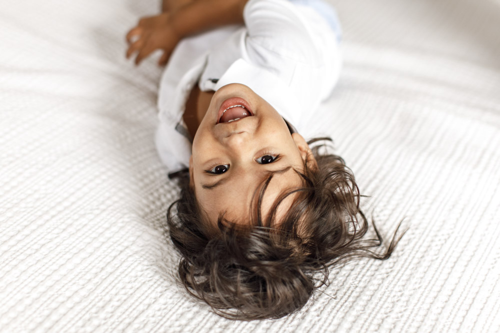 close up of toddler lying on the bed smiling at the camera upside down