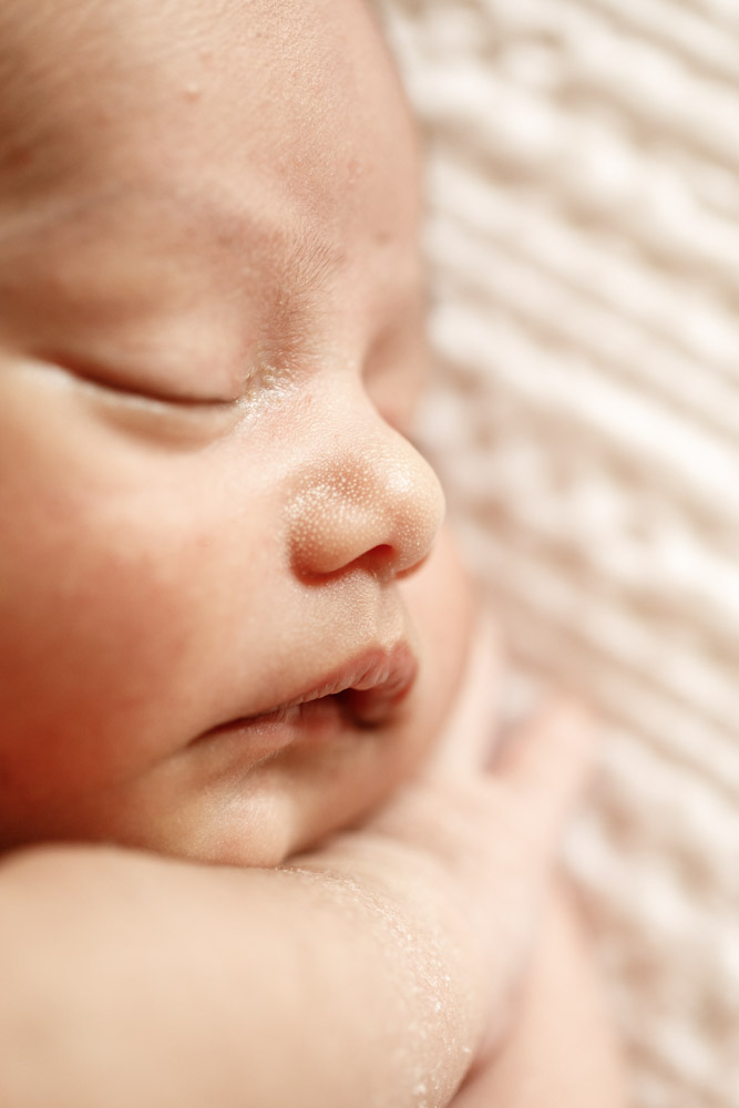 close up of baby's face hand tucked under its chin while sleeping on its left side