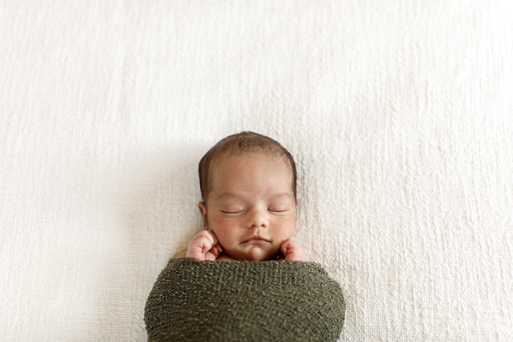close up of a newborn swaddled in a green blanket with its hands sticking out eyes closed