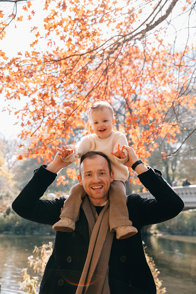 daughter sitting on her fathers shoulders in Central Park in a Fall mood