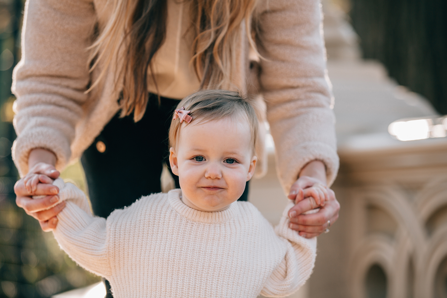 close up of a little girl smiling at the camera while mom is holding her hands in Central Park