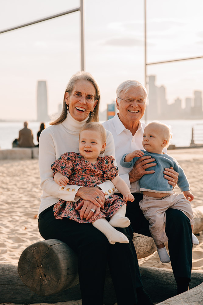 grandbabies sitting in grandparents lap smiling at the camera with Manhattan skyline in the background