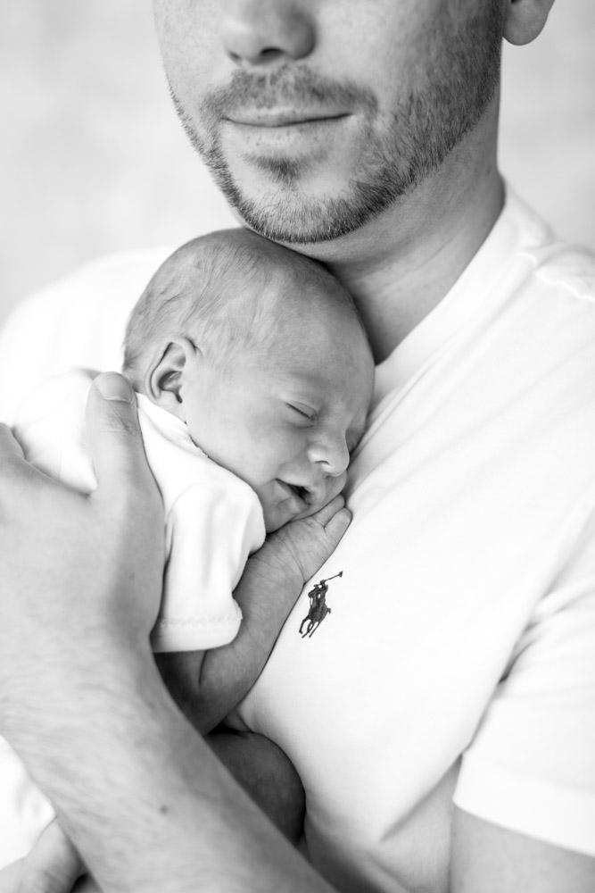 black and white photo of father holding the sleeping and smiling newborn close to his chest