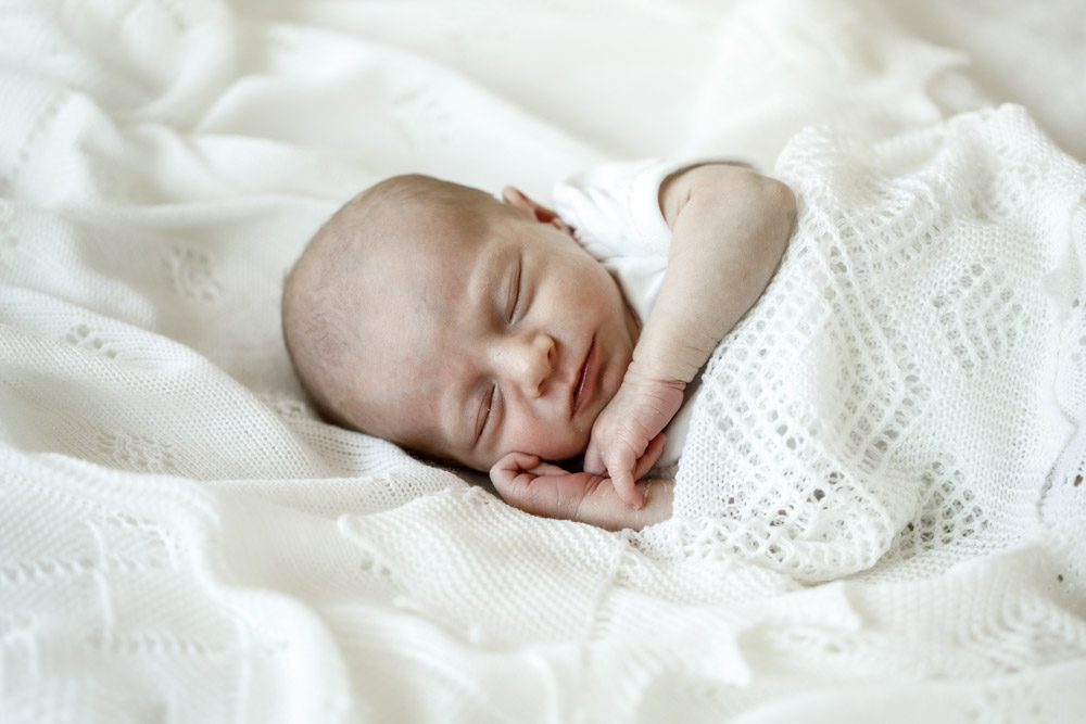 newborn sleeping on its side with hand tucked under the chin wrapped up in a white blanket