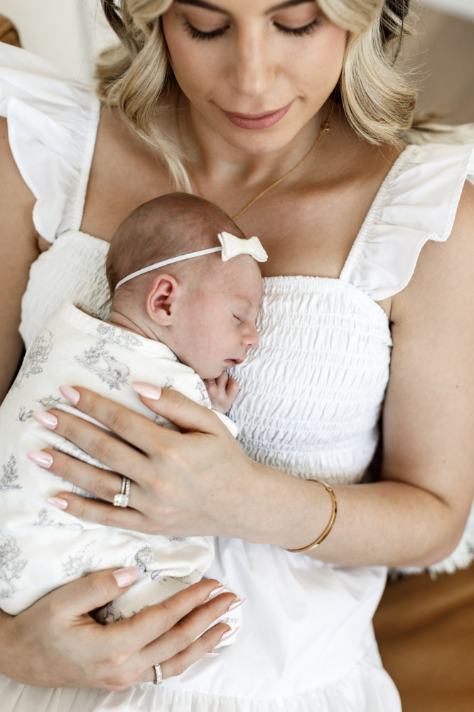mother in beautiful white dress is holding her newborn close to her chest