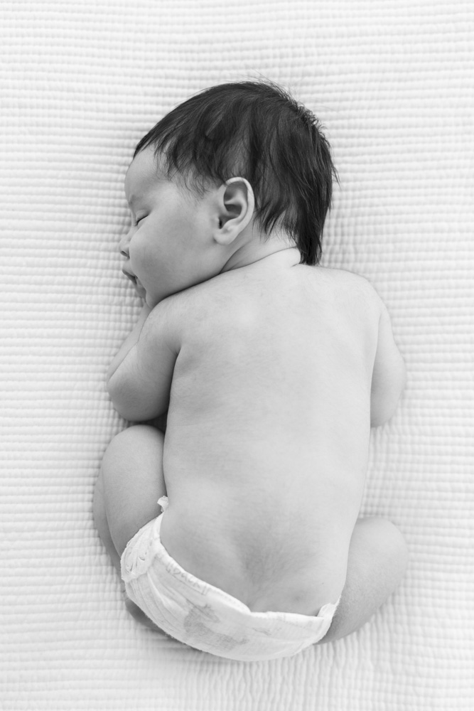 black and white photo of newborn lying in a frog pose with hand tucked under its chin in bird's eye perspective