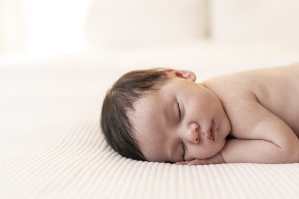 close up of a sleeping newborn lying on its side with hand tucked under the chin on a white blanket
