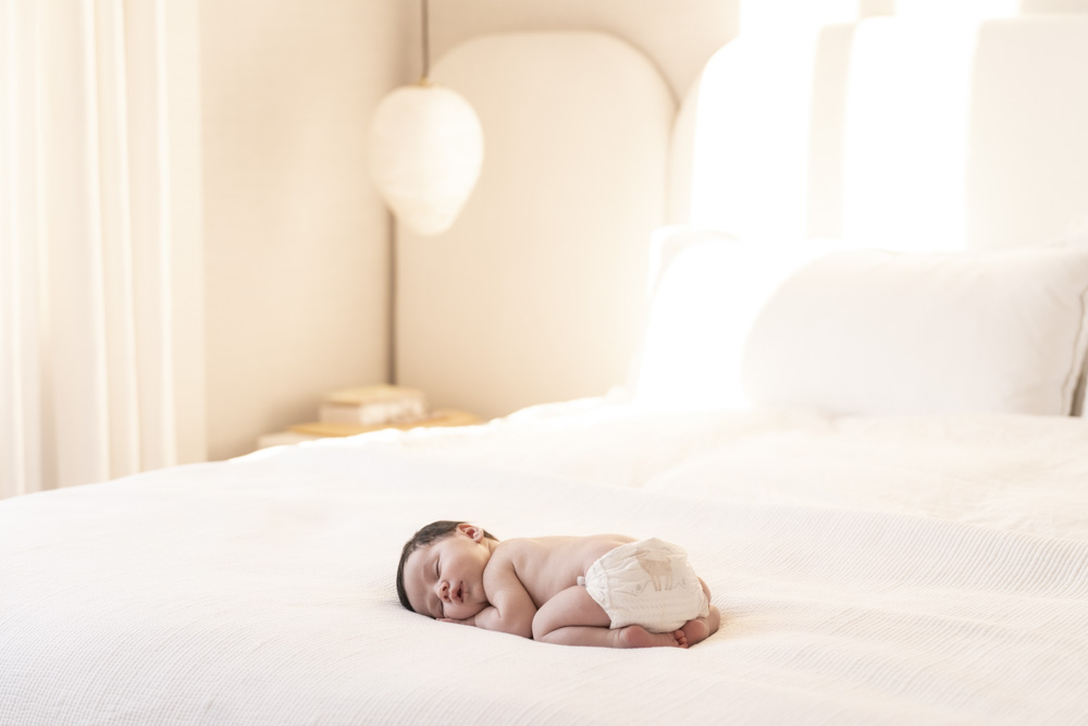 sleeping newborn wearing diapers lying on a big bed with white sheets
