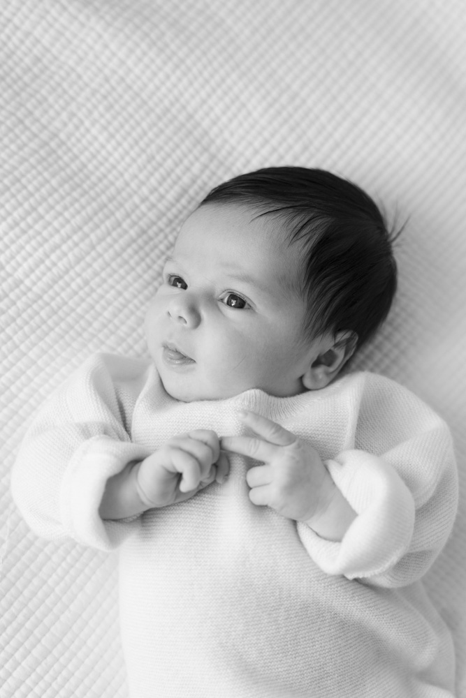 black and white photo of a newborn with dark hair lying on a white blanket