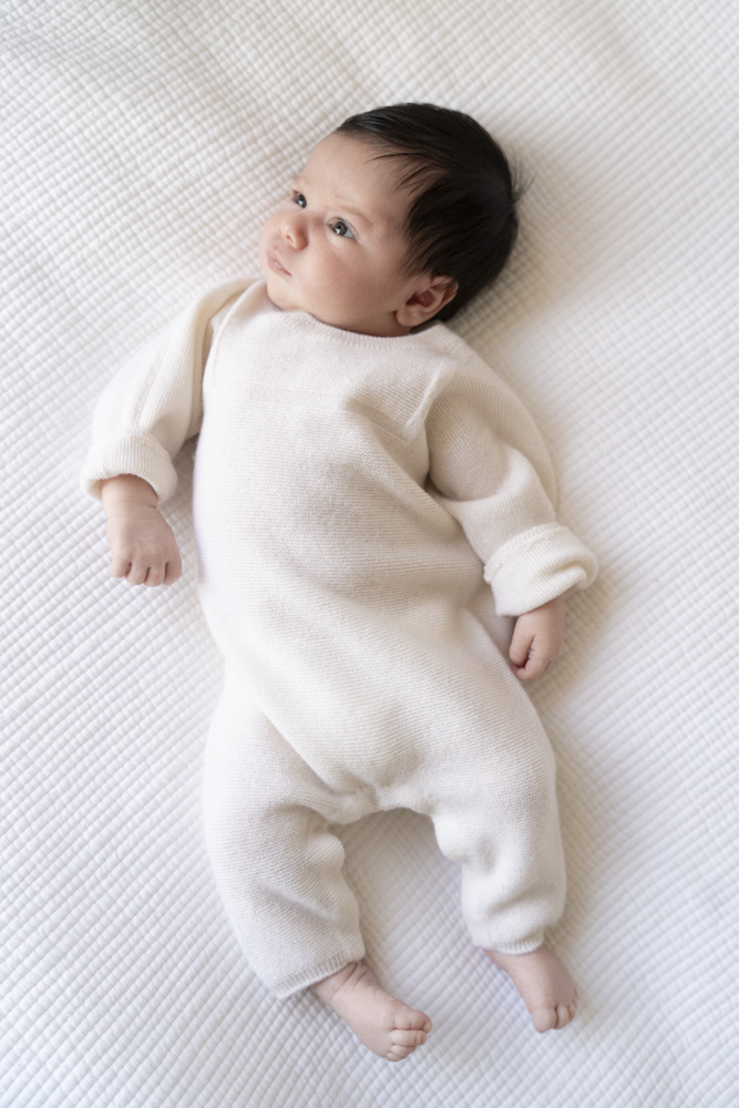 newborn with dark hair wearing a white onesie lying on a white blanket eyes open
