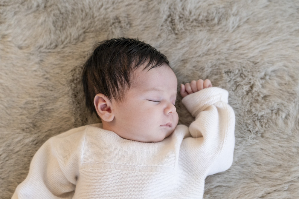 close up of sleeping newborn wearing a white shirt lying on a grey blanket looking to the side