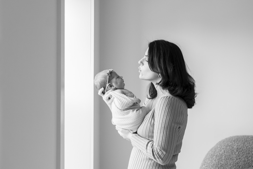 black and white photo of mother holding her newborn in front of her both looking at each other