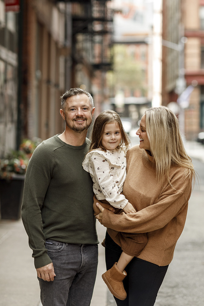 family of three in the streets of New York while mother is holding her daughter and smiling at her