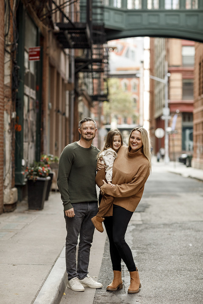 family of three in the streets of New York smiling at the camera while mother is holding her daughter
