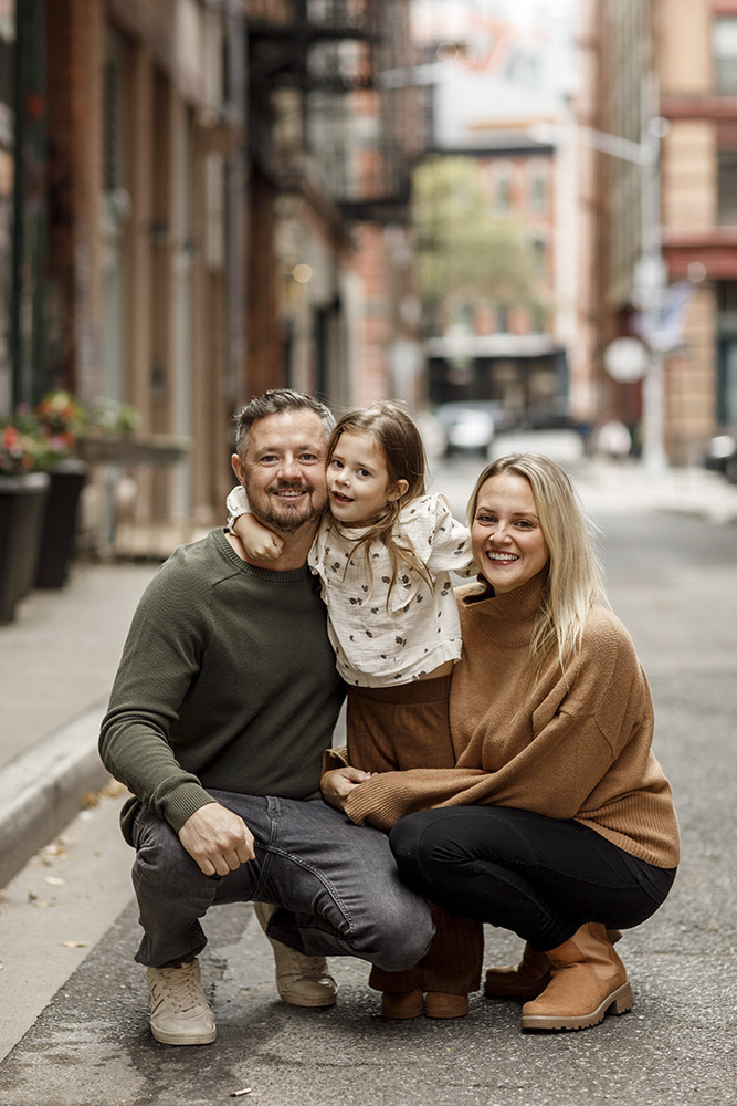 family of three in the streets of New York smiling at the camera while daughter is standing in the middle