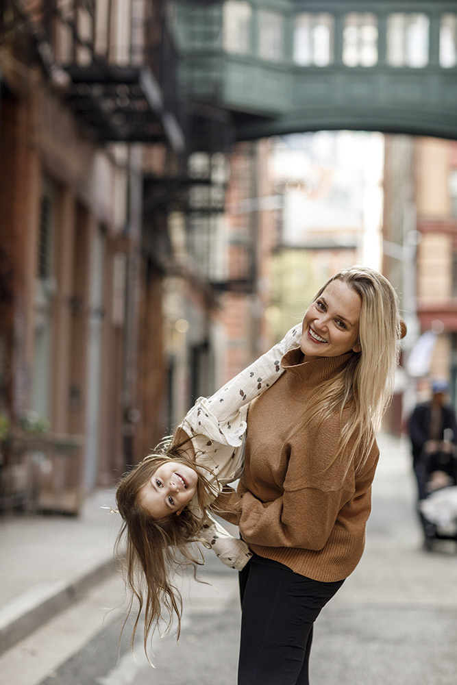 mother is holding her daughter and swirling her around in the streets of New York daughter's hair is flying both are smiling at the camera