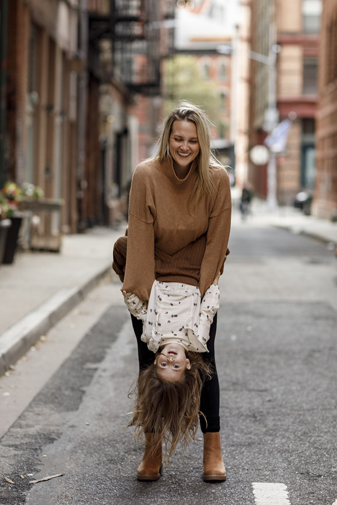 mother is holding her daughter upside down in the streets of New York daughter is looking at the camera while mom is smiling at her