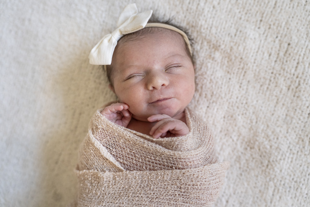 close up of a sleeping newborn swaddled in a beige blanket wearing a headband