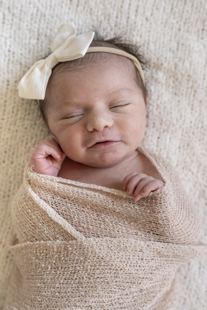 close up of a sleeping newborn swaddled in a beige blanket wearing a headband