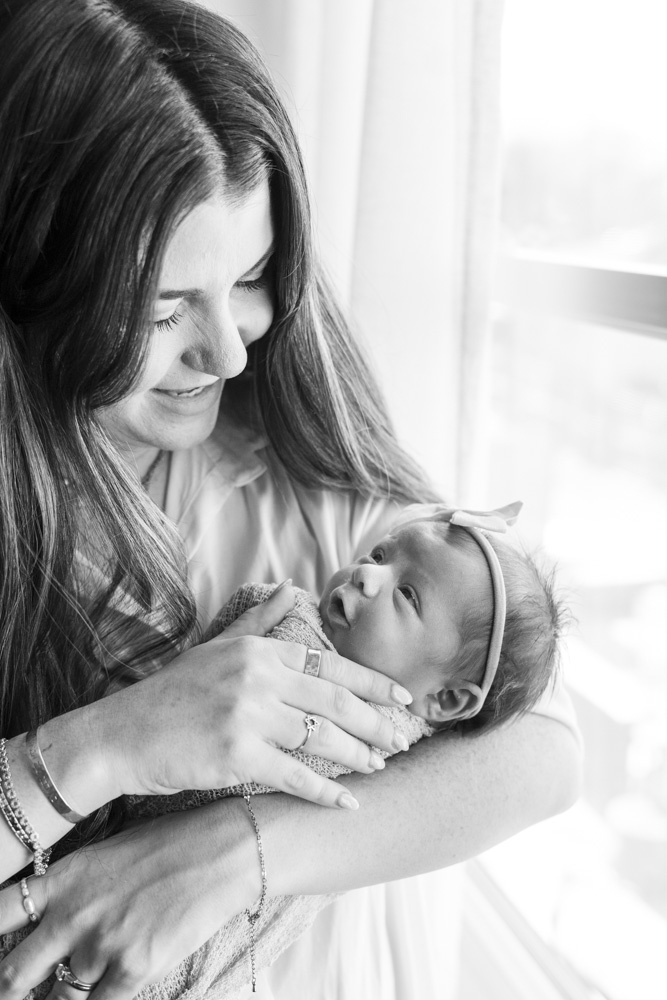 black and white photo of mother holding her newborn while newborn is smiling at her