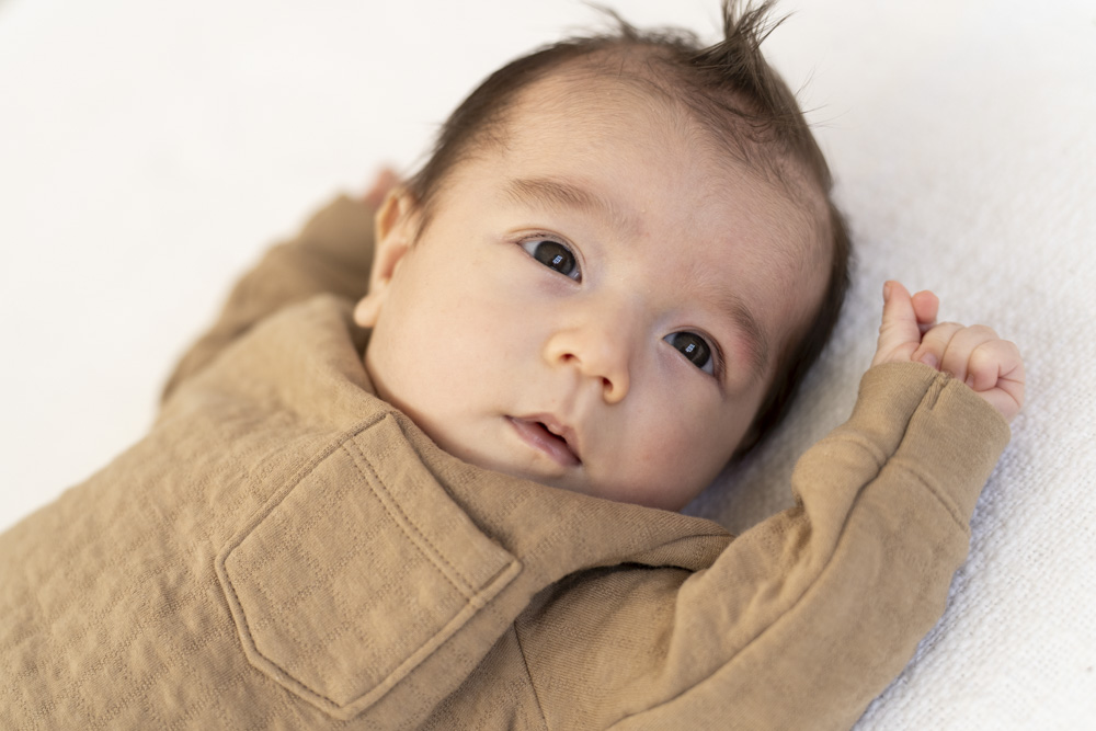 close up of newborn wearing a brown shirt lying on its back with eyes wide open