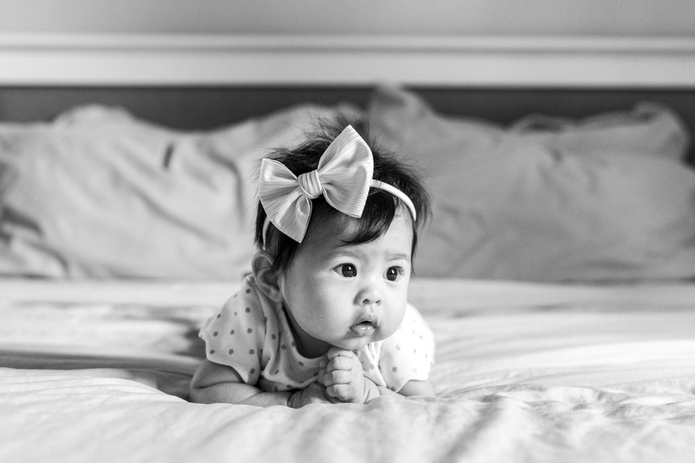 Baby Session, black and white photo of baby girl lying on her belly wearing a big bow headband looking to the side