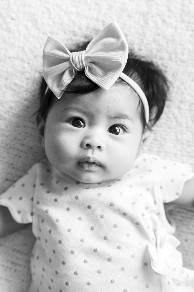 Baby Session, black and white photo of newborn baby girl wearing a polka dot dress and a bow headband looking at the camera