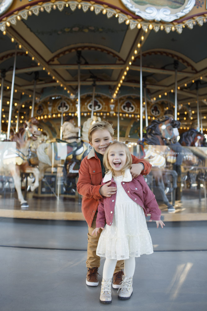 Family Session, brother and sister hugging each other front of a beautiful old carousel