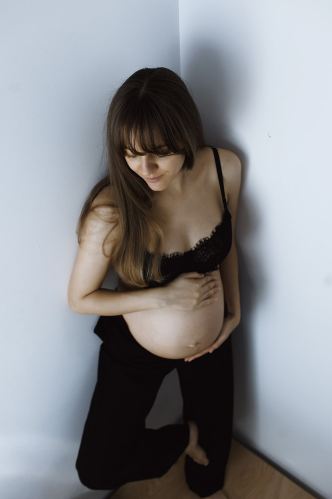 Maternity Photos, pregnant woman standing in the corner holding her belly wearing black pants and a black top