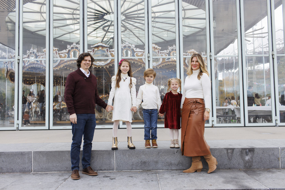 Family Photography, family of five are standing next to each other and holding hands in front of an old beautiful old carousel