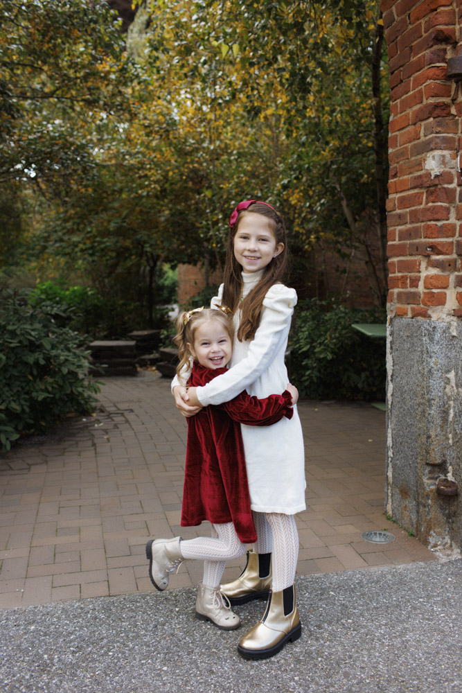 Family Photography, two little sisters in beautiful dresses standing in a park hugging each other