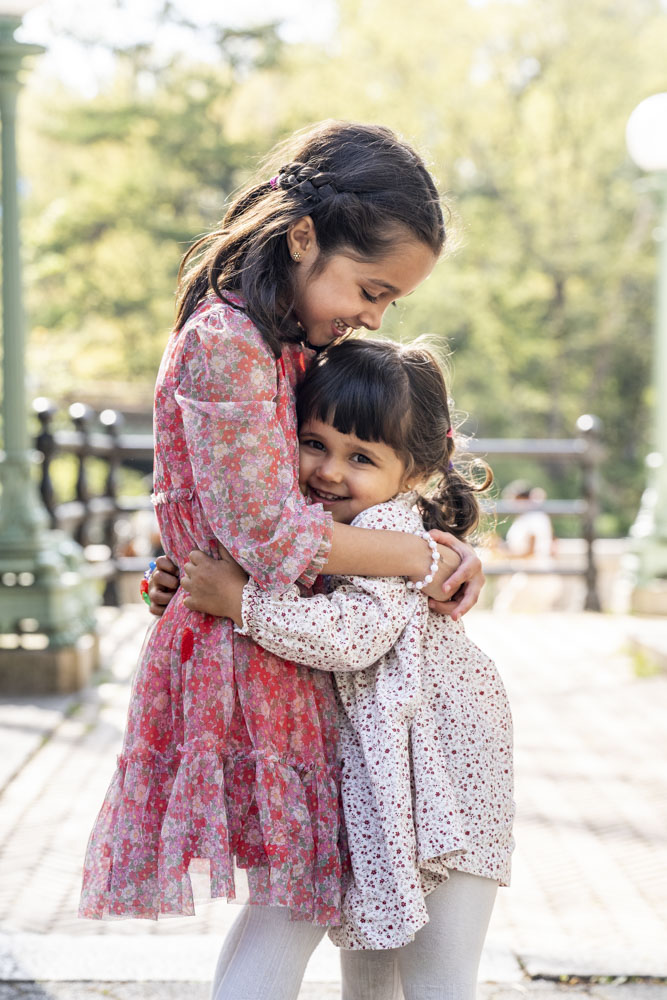Family Session, two sisters in beautiful dresses hugging each other in a park