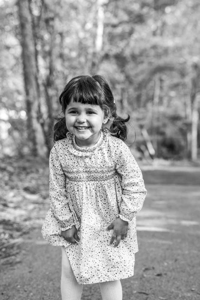 Family Photography, black and white photo of a beautiful little girl with side braids in a park wearing a pretty dress smiling big