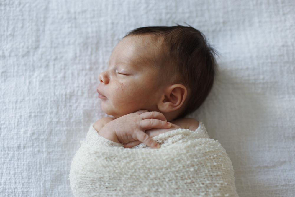 Baby Photography, close up of a newborn swaddled in a beige blanket with its hands sticking out eyes closed