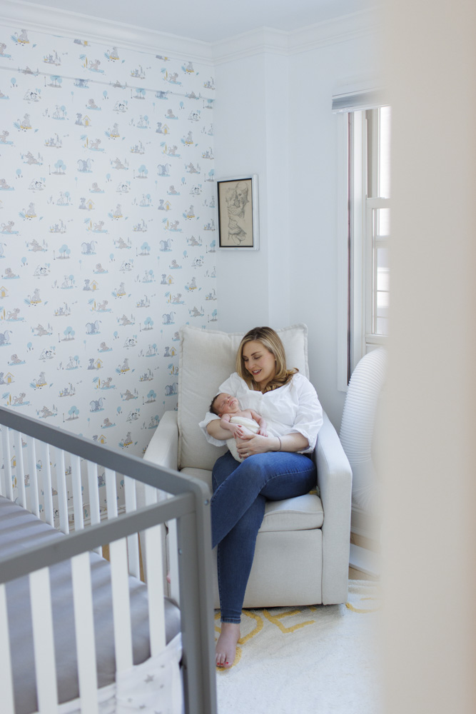 Newborn Photography, mother in a white shirt and blue jeans is sitting in a comfortable chair in the nursery holding her newborn in her arms