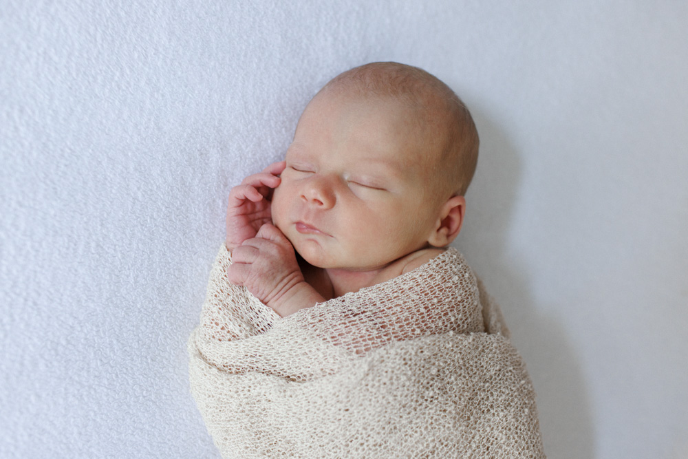 Baby Photography, close up of a newborn swaddled in a beige blanket with its hands sticking out eyes closed