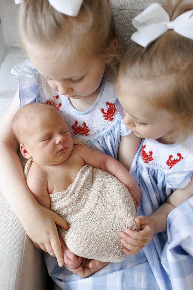 Family Session, proud sisters in beautiful dresses are holding their sleeping newborn sibling
