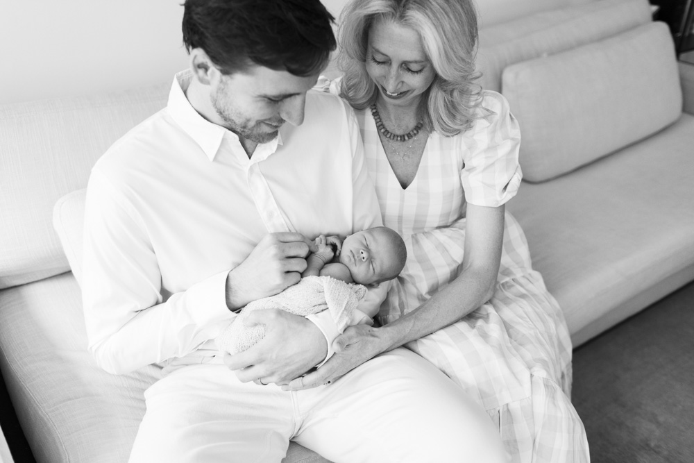 Baby Photography, black and white photo of mom and dad sitting on the couch while dad is holding the newborn baby