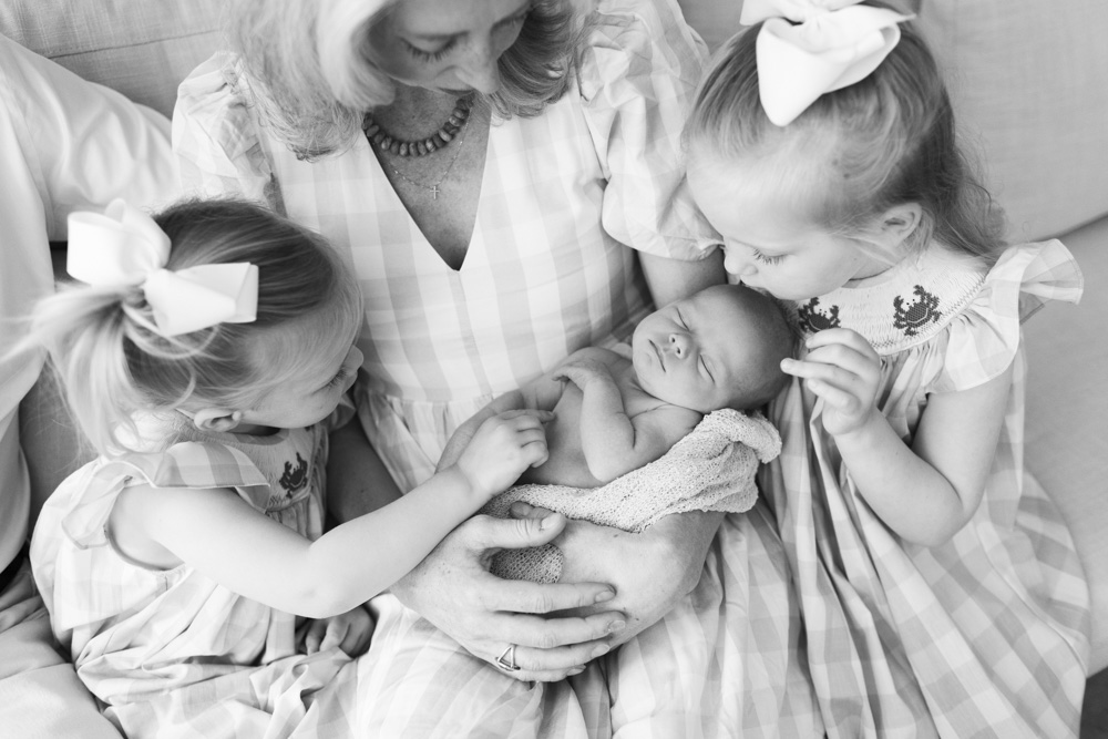 Family Session, black and white photo of mother holding her newborn baby surrounded by her two daughters who are hugging and touching their sibling