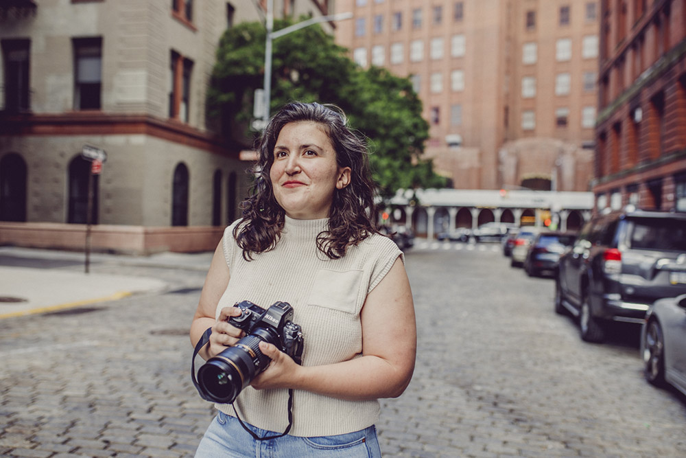 Baby Photography, woman with dark longer hair holding a camera is standing in the streets of Manhattan
